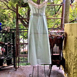 May include: A vintage-style, off-the-shoulder dress with horizontal stripes in light green and white. The dress is displayed on a metal dress form, showcasing its design and fit. The neckline is adorned with delicate lace trim.