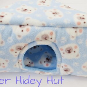 May include: A blue corner hidey hut for small pets, patterned with white polar bear faces with pink details. The triangular hut has an arched entrance. The text "Corner Hidey Hut" is visible at the bottom. The hut is designed for small pets.
