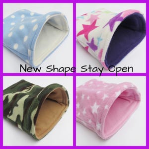 May include: Four different fleece pet beds in various colours and patterns. The beds are shaped like a tube with an opening at one end. The patterns include blue with white polka dots, pink with white stars, camouflage, and white with pink and purple stars. The text "New Shape Stay Open" is printed below the beds.