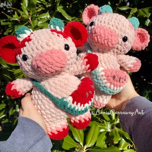 Pode incluir: Dois brinquedos de pel&uacute;cia de croch&ecirc; em forma de porcos, um rosa com um design de melancia verde e vermelho e o outro rosa com um design de morango verde e vermelho.