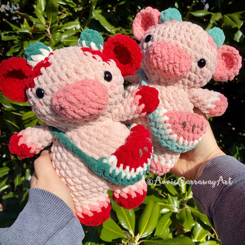 Pode incluir: Dois brinquedos de pel&uacute;cia de croch&ecirc; em forma de porcos, um rosa com um design de melancia verde e vermelho e o outro rosa com um design de morango verde e vermelho.