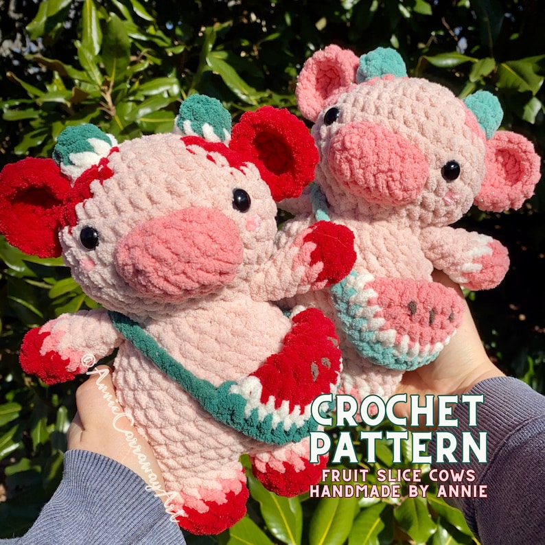 Pode incluir: Dois peluches de vaca rosa em croch&ecirc; com detalhes vermelhos e verdes. Cada vaca segura uma fatia de fruta em croch&ecirc;, uma melancia e um morango. O texto "CROCHET PATTERN FRUIT SLICE COWS HANDMADE BY ANNIE" est&aacute; na parte inferior da imagem.