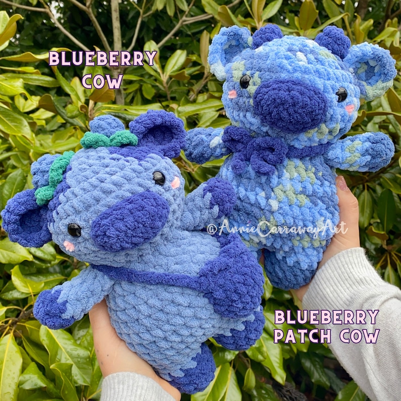 Puede incluir: Dos peluches de vaca de ar&aacute;ndano tejidos a crochet. Uno es de color azul s&oacute;lido y el otro tiene un dise&ntilde;o de patchwork con hilo azul, verde y blanco. Los peluches tienen ojos negros, mejillas rosadas y un lazo verde.