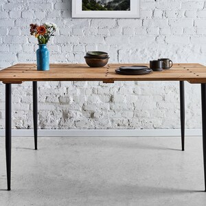 Puede incluir: Una mesa de comedor de madera con un acabado r&uacute;stico y patas de metal negro. La mesa est&aacute; puesta con un jarr&oacute;n de flores, platos y tazas.