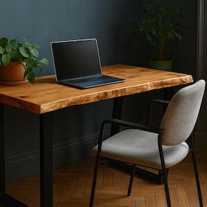 Peut inclure: Un bureau en bois avec un bord brut et des pieds en métal noir. Un ordinateur portable est posé sur le bureau, et une chaise grise est placée à proximité. Une plante en pot ajoute une touche de verdure.