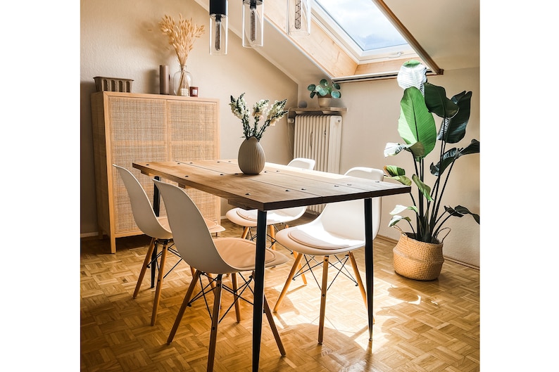 Puede incluir: Una mesa de comedor de madera con patas de metal negro y cuatro sillas blancas. La mesa est&aacute; puesta con un jarr&oacute;n de flores blancas y una planta en una cesta tejida.