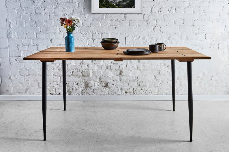 Puede incluir: Una mesa de comedor de madera con un acabado r&uacute;stico y patas de metal negro. La mesa est&aacute; puesta con un jarr&oacute;n de flores, platos y tazas.