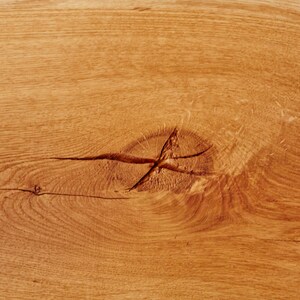 May include: Close-up of a light brown wood surface with a knot in the center. The wood grain is visible and the surface is smooth.