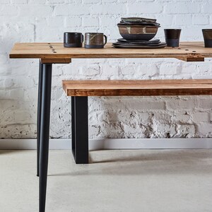 Puede incluir: Una mesa de comedor de madera con patas de metal negro y un banco de madera a juego. La mesa est&aacute; puesta con un taz&oacute;n, platos y tazas.