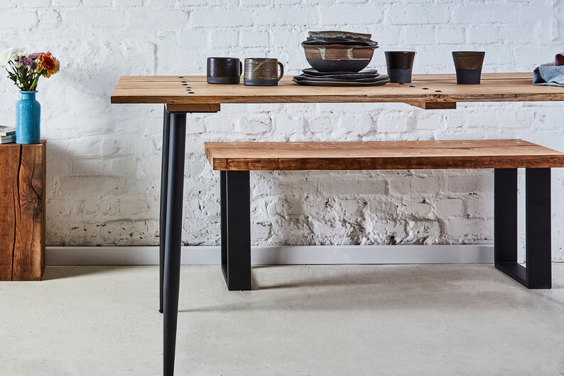 Puede incluir: Una mesa de comedor de madera con patas de metal negro y un banco de madera a juego. La mesa est&aacute; puesta con un taz&oacute;n, platos y tazas.
