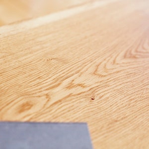 May include: Close-up of a light brown wood surface with a natural wood grain pattern. The surface is smooth and has a slight sheen.