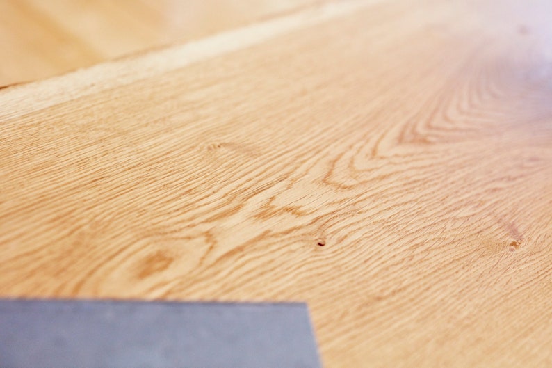 May include: Close-up of a light brown wood surface with a natural wood grain pattern. The surface is smooth and has a slight sheen.