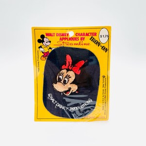 May include: A vintage iron-on applique featuring Minnie Mouse with a red bow. The applique is on a navy blue background, packaged in a yellow and black card with the text "WALT DISNEY CHARACTER APPLIQUES BY Streamline".