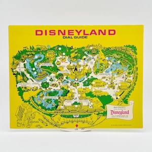 May include: A yellow Disneyland Dial Guide featuring a detailed green map of the park with various attractions labeled. The text reads Disneyland Dial Guide and Walt Disney's Dial Guide to Disneyland. It includes small circular cutouts across the map.