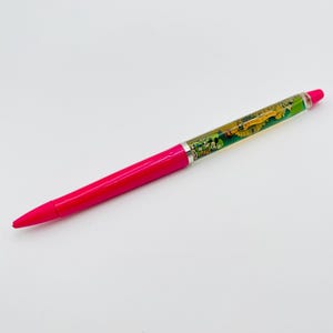 May include: A retractable ballpoint pen with a bright pink lower barrel and a clear upper barrel containing a floating graphic insert. The insert features a colorful illustration of Mickey Mouse and the text 35 YEARS OF MAGIC in yellow.