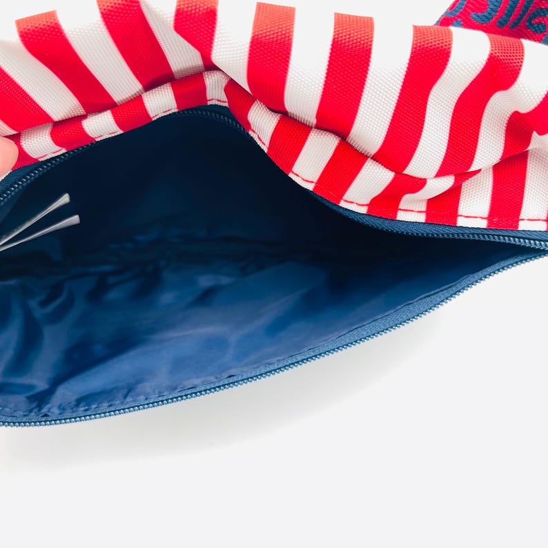 Puede incluir: Bolso abierto con rayas rojas y blancas y un interior azul. El bolso tiene un cierre de cremallera azul. El bolso est&aacute; hecho de un material resistente.
