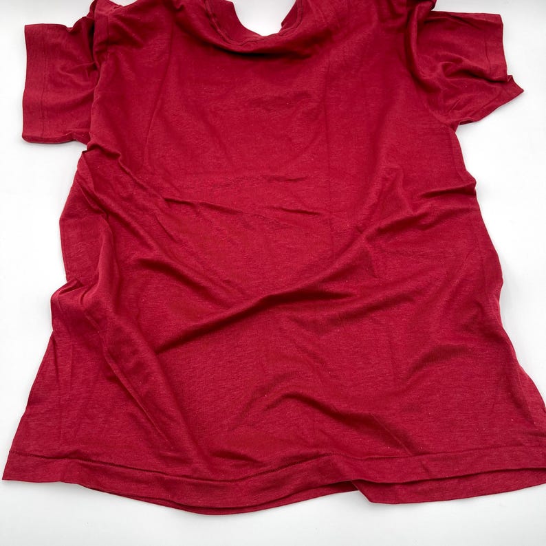 May include: A solid red short-sleeved t-shirt with a crew neckline. The garment features a plain, unpatterned design with visible fabric folds and a standard hemline at the sleeves and bottom, presented in a flat, unfolded orientation.