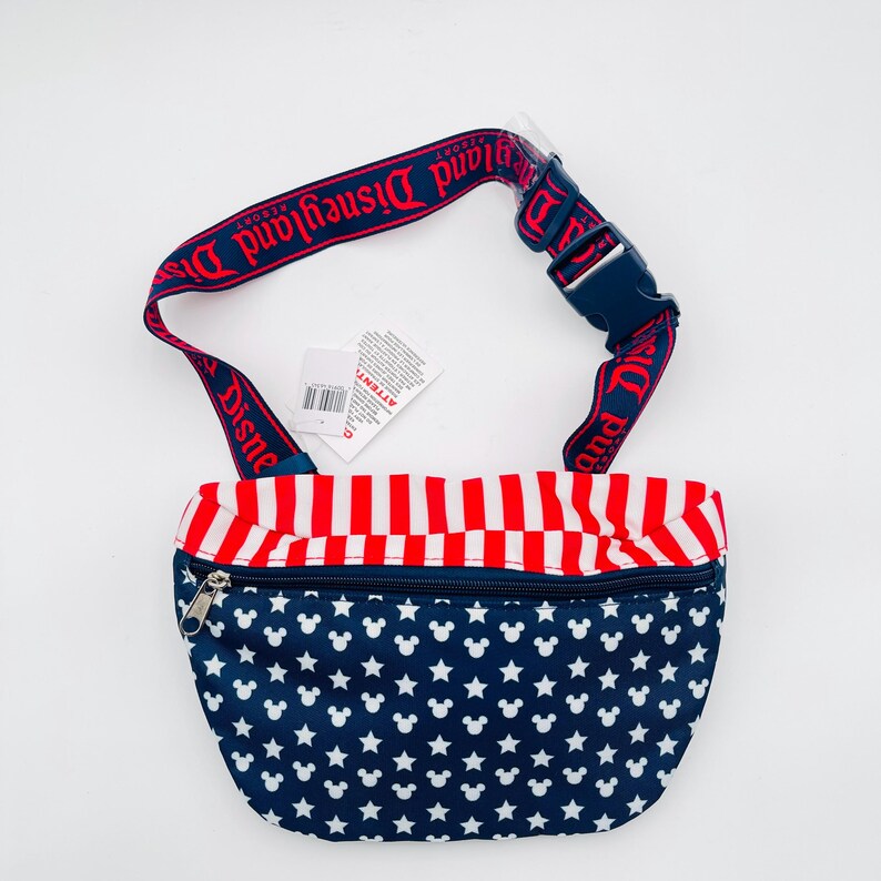 Puede incluir: Ri&ntilde;onera azul marino con cabezas de Mickey Mouse y estrellas blancas. La parte superior tiene rayas rojas y blancas. La correa ajustable es roja con "Disneyland Resort" impreso en blanco. Hebilla azul.