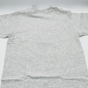 May include: A short-sleeved t-shirt in a light heather gray color. The garment features a classic crew neckline and a standard fit with visible fabric texture throughout. The material has a speckled appearance with darker gray flecks.