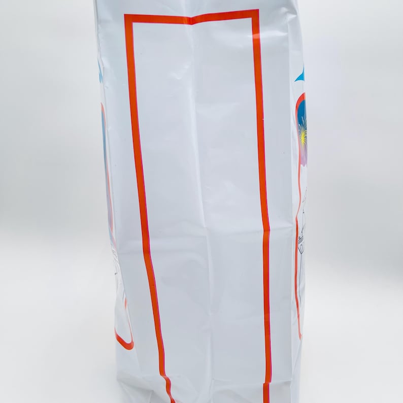 May include: A tall white rectangular plastic bag featuring a prominent vertical orange rectangular border on the front surface. The sides of the bag display partial blue and red graphic elements with thin line drawings of fireworks and star shapes.