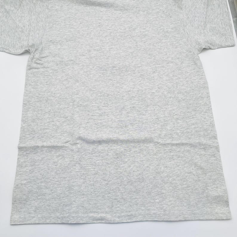 May include: A short-sleeved t-shirt in a light gray heathered fabric. The garment features a classic crew neckline and a standard straight hemline. The material displays a subtle speckled texture throughout, consistent with a heathered cotton blend.