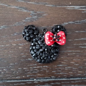 May include: Black rhinestone Mickey Mouse head charm with a red bow. The bow has white polka dots.