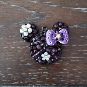 Pu&ograve; includere: Un ciondolo Mickey Mouse in strass nero e viola con un fiocco viola.