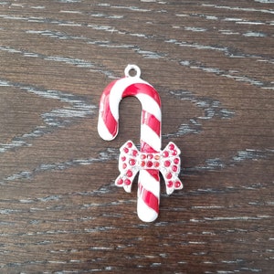May include: A red and white candy cane charm with a red rhinestone bow. The charm is made of metal and has a silver finish.