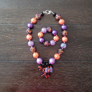 May include: A purple, orange, and black beaded necklace with a matching bracelet and a black, orange, and purple Minnie Mouse head charm.