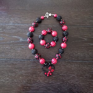 May include: A red and black polka dot necklace and bracelet set with a black and red Minnie Mouse charm.