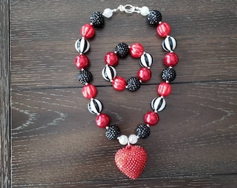 May include: A red and black beaded necklace with a large red heart pendant. The necklace is paired with a matching red and black beaded bracelet.