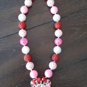 May include: A pink, white, and red beaded necklace with a rhinestone Minnie Mouse charm. The beads are various sizes and have different patterns, including hearts and polka dots.