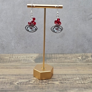 May include: Silver football earrings with red crystal accents. The football charm features the Kansas City Chiefs logo.