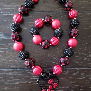 May include: A red and black beaded necklace and bracelet set with a Minnie Mouse charm. The necklace and bracelet are made with large, chunky beads and have a silver clasp.