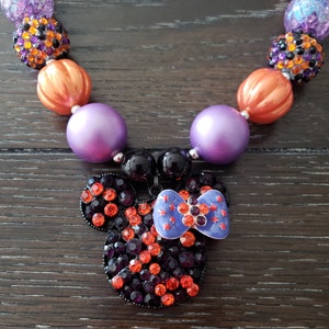 May include: A Halloween-themed necklace with orange, purple, and black beads, featuring a rhinestone Mickey Mouse head with a purple bow.