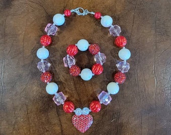 May include: A red and white beaded necklace with a red rhinestone heart pendant and a matching red and white beaded bracelet.