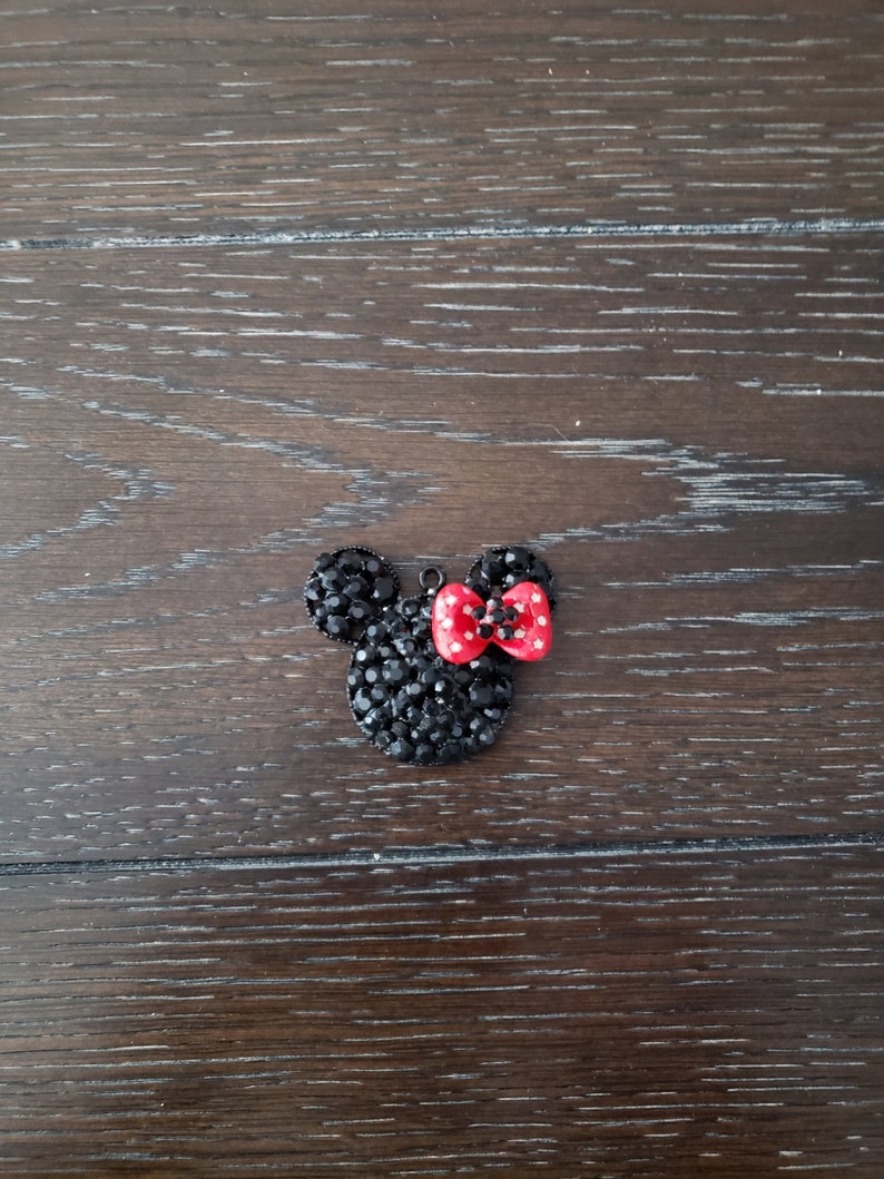 May include: Black rhinestone Mickey Mouse head charm with a red bow. The bow has white polka dots.