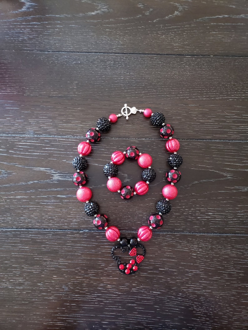 May include: A red and black polka dot necklace and bracelet set with a black and red Minnie Mouse charm.