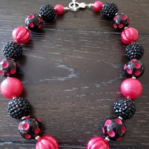 May include: A black and red chunky necklace with a large black and red ladybug charm. The necklace is made of large, round beads with a variety of textures, including smooth, textured, and sparkly.