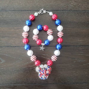 May include: A red, white, and blue beaded necklace and bracelet set. The necklace has a Mickey Mouse pendant with red, white, and blue rhinestones. The bracelet has a silver star charm.