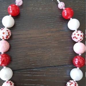 Pode incluir: Um colar de contas grossas vermelho, branco e rosa com fechos prateados. As contas s&atilde;o grandes e t&ecirc;m uma variedade de texturas, incluindo lisas, brilhantes e texturizadas.