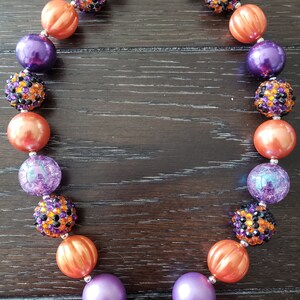 May include: A Halloween-themed necklace with orange, purple, and black beads. The beads are decorated with rhinestones and glitter. The necklace has a silver clasp.