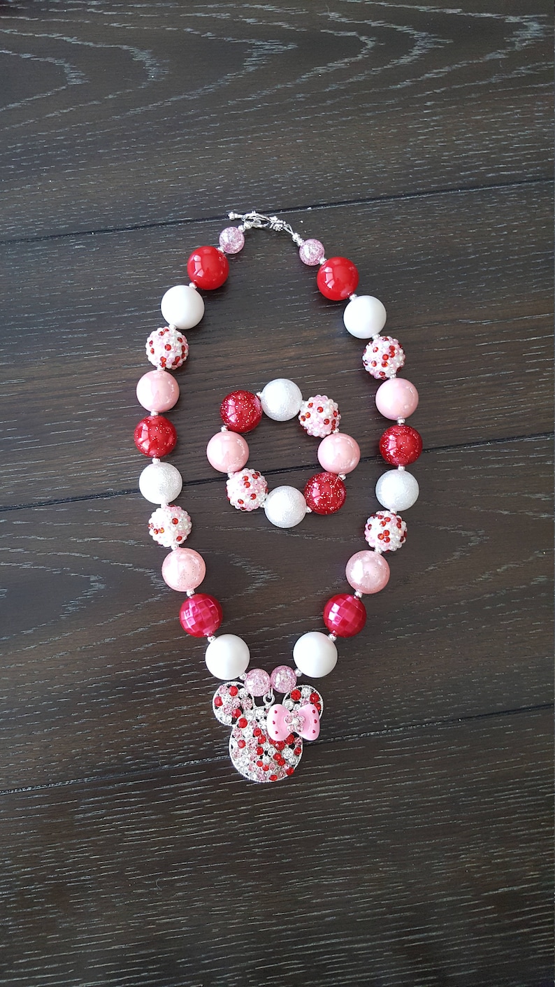 Pode incluir: Um colar de contas vermelhas, cor-de-rosa e brancas com um amuleto de Minnie Mouse de strass. O colar vem com uma pulseira combinando.