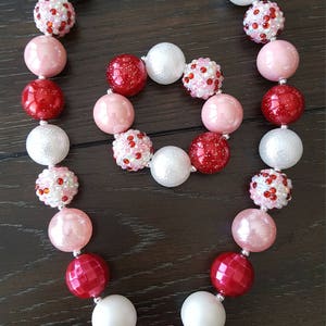 Pode incluir: Um colar de contas grossas vermelho, branco e rosa com um fecho prateado e um pingente de Minnie Mouse de strass. O colar vem com uma pulseira combinando.