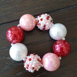 Pode incluir: Um bracelete de contas rosa, vermelho e branco com contas brilhantes.