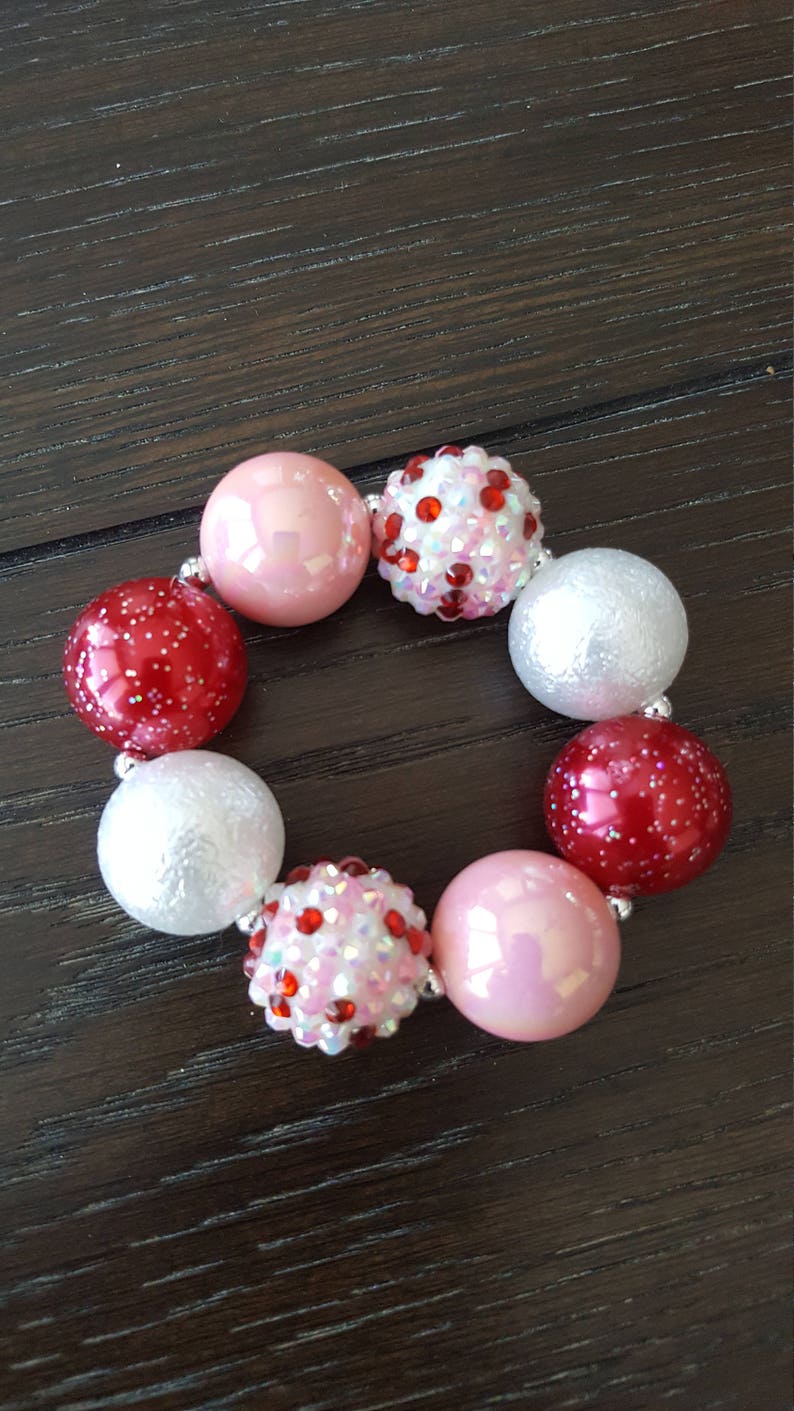 Pode incluir: Um bracelete de contas rosa, vermelho e branco com contas brilhantes.