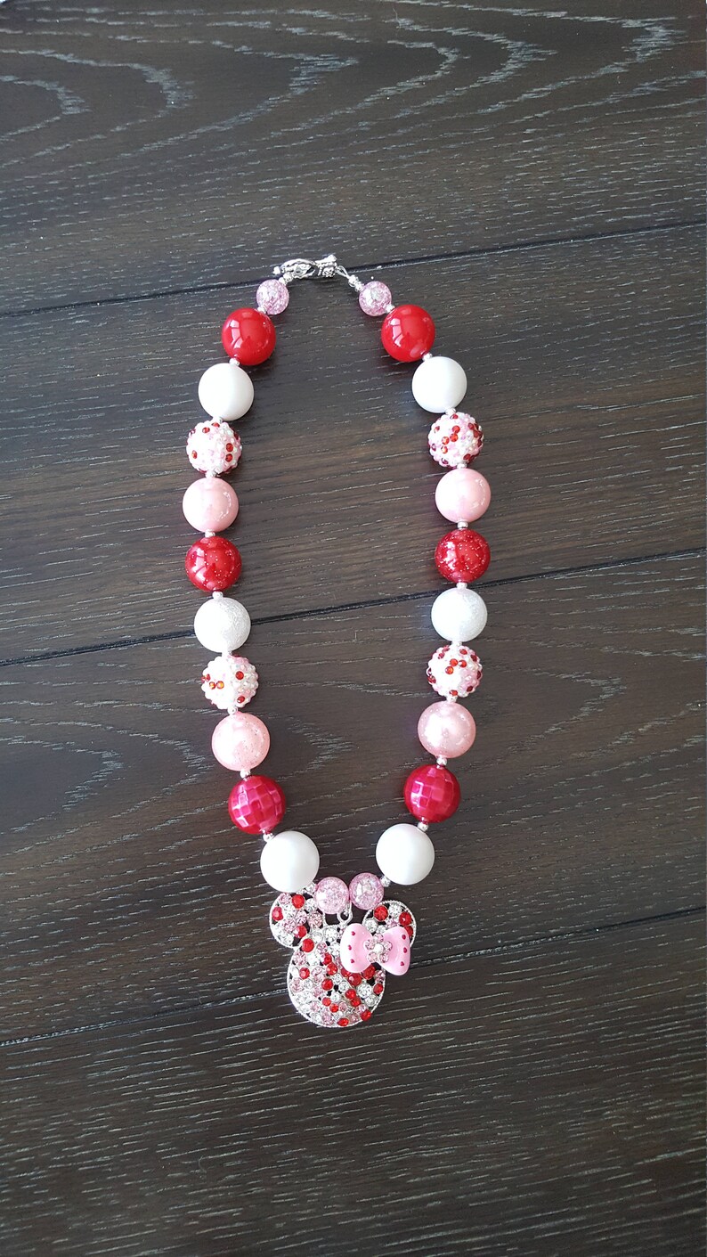Pode incluir: Um colar de contas grossas vermelho, rosa e branco com um pingente de Minnie Mouse de strass.