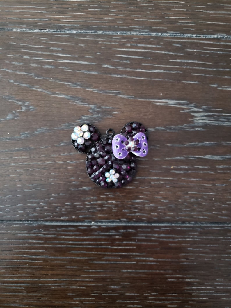 Pu&ograve; includere: Un ciondolo Mickey Mouse in strass nero e viola con un fiocco viola.