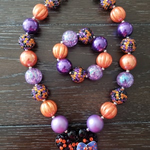 May include: A purple and orange beaded necklace with a black and purple Minnie Mouse charm. The necklace is made of large, chunky beads and has a silver clasp.