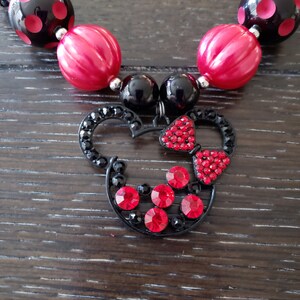 May include: A black and red beaded necklace with a Minnie Mouse charm. The charm is made of black metal and has red rhinestones.